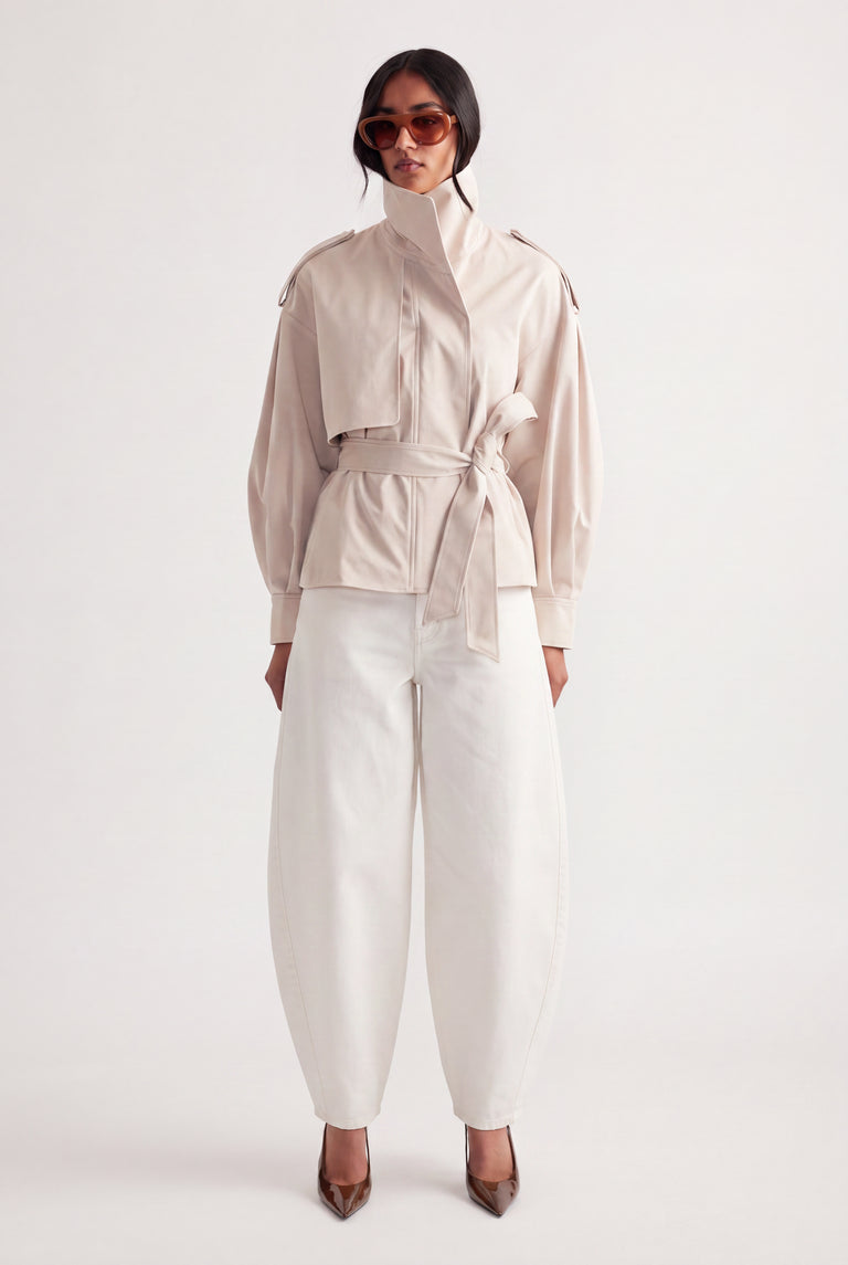 Woman wearing white mid rise barrel jeans with a belted cream jacket and pointed heels