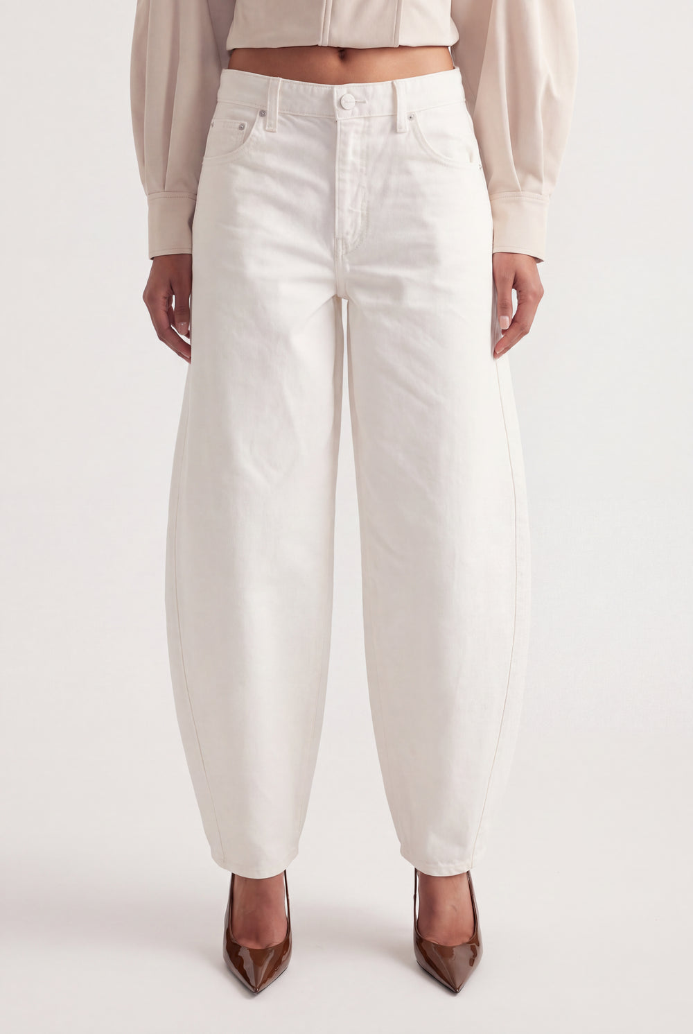 Woman wearing white mid rise barrel leg jeans with sculptural seams, a cropped top and pointed heels