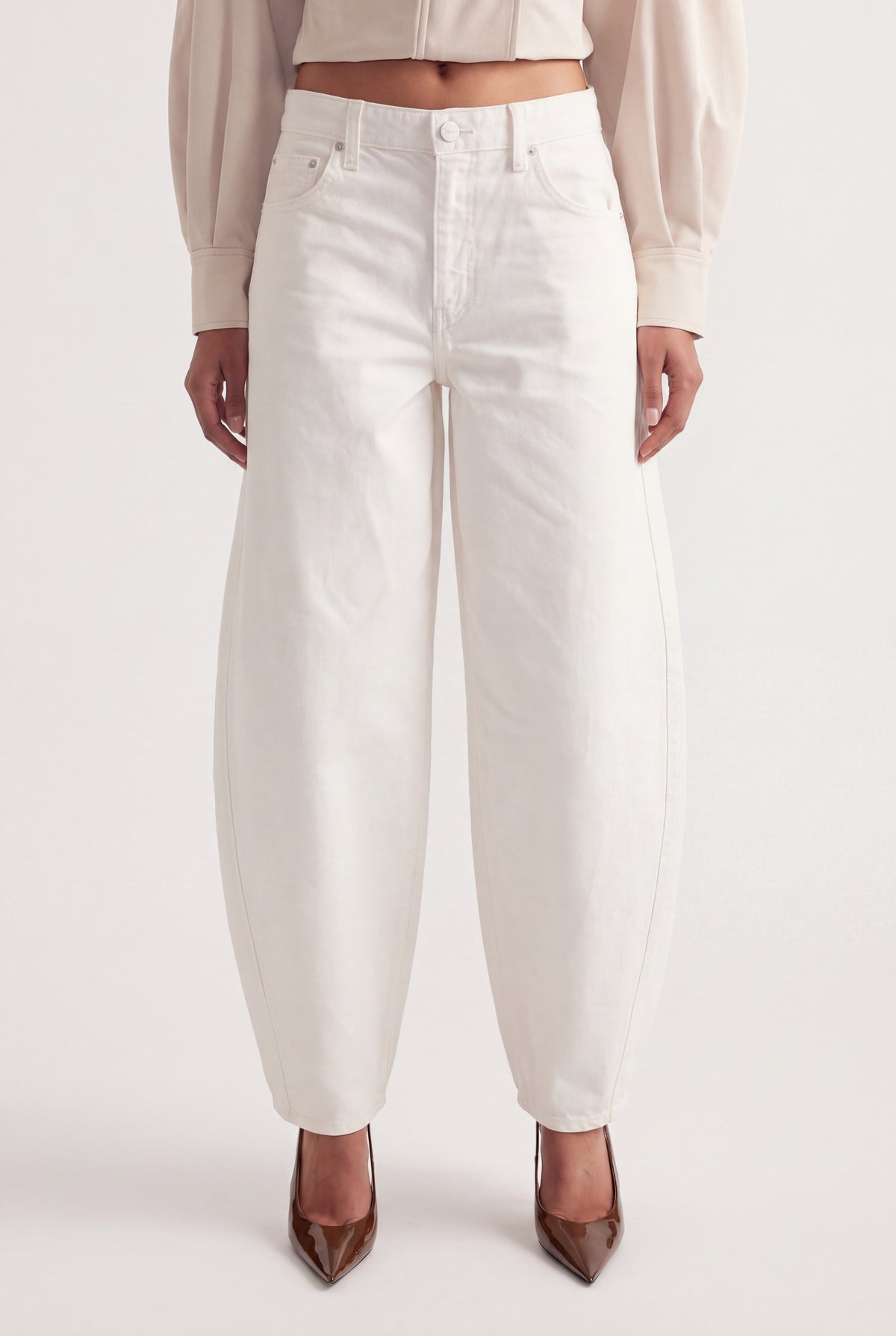 Woman wearing white mid rise barrel leg jeans with sculptural seams, a cropped top and pointed heels