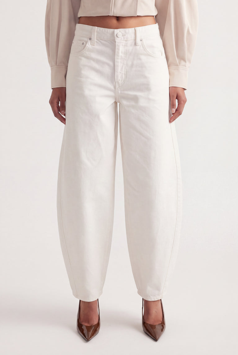 Woman wearing white mid rise barrel leg jeans with sculptural seams, a cropped top and pointed heels