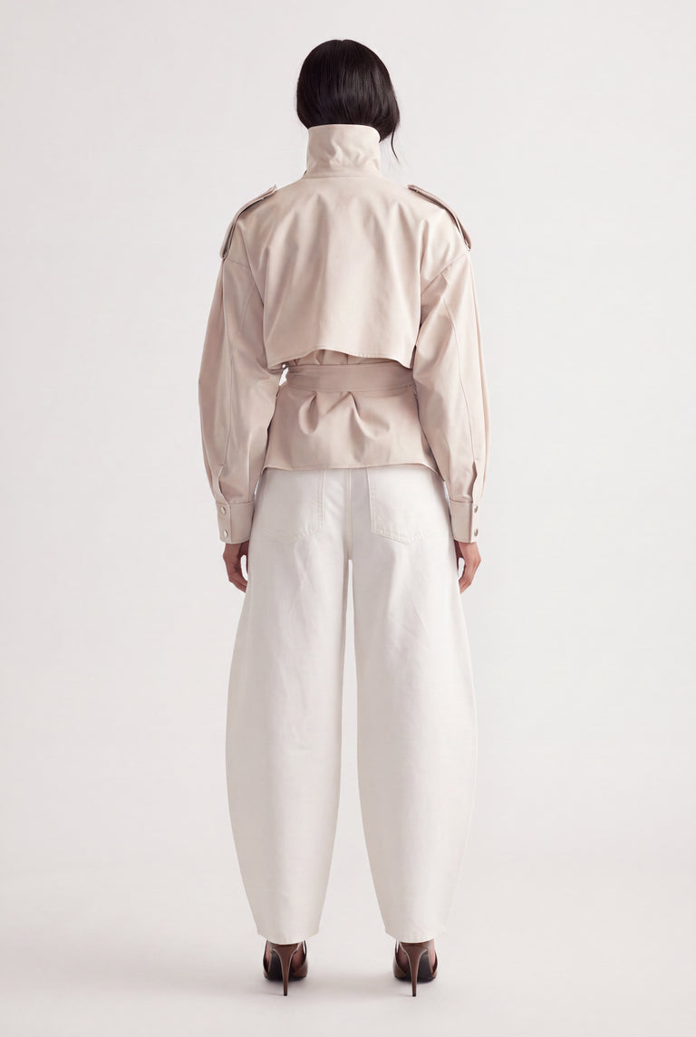 Back view of woman wearing white barrel leg jeans with a cropped beige jacket and heeled boots