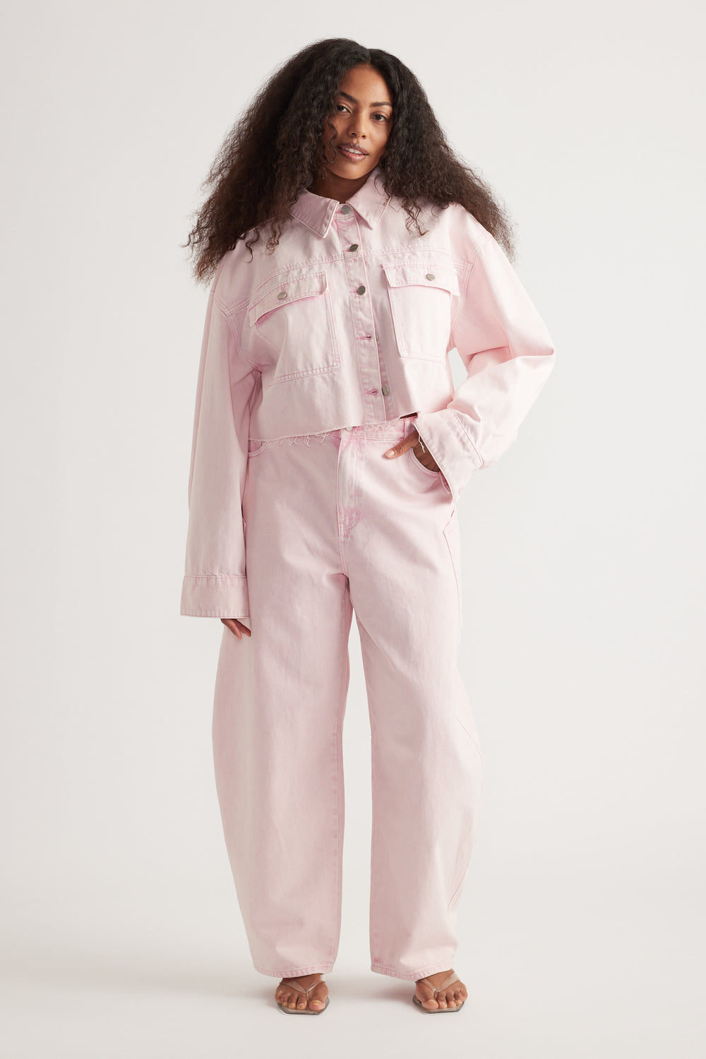 Woman wearing a pink denim jacket with matching barrel-leg jeans and sandals