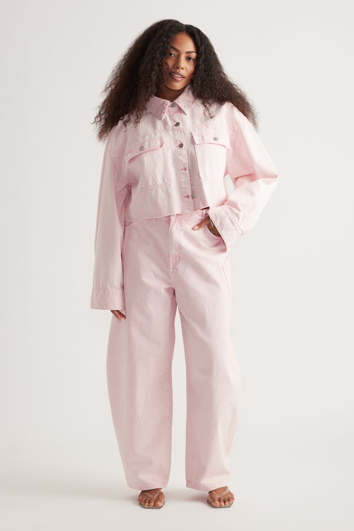 Woman wearing a pink denim jacket with matching barrel-leg jeans and sandals