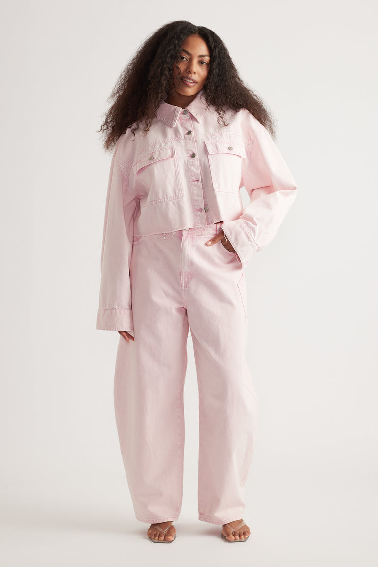 Woman wearing a pink denim jacket with matching barrel-leg jeans and sandals