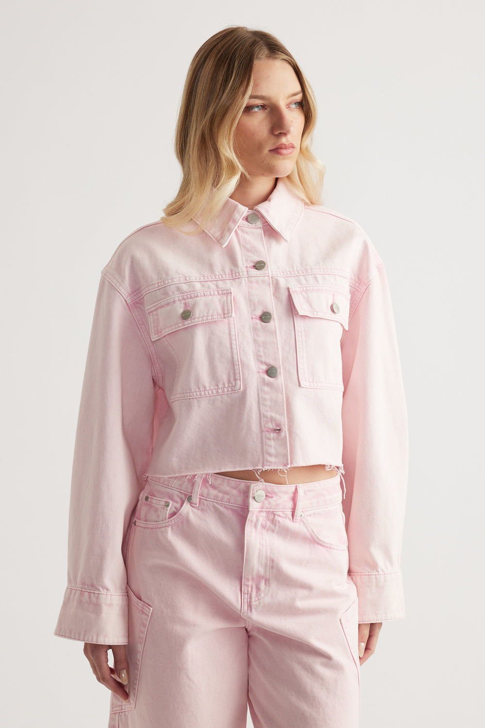 Woman wearing a pink cropped denim shirt with patch pockets and matching high waisted jeans