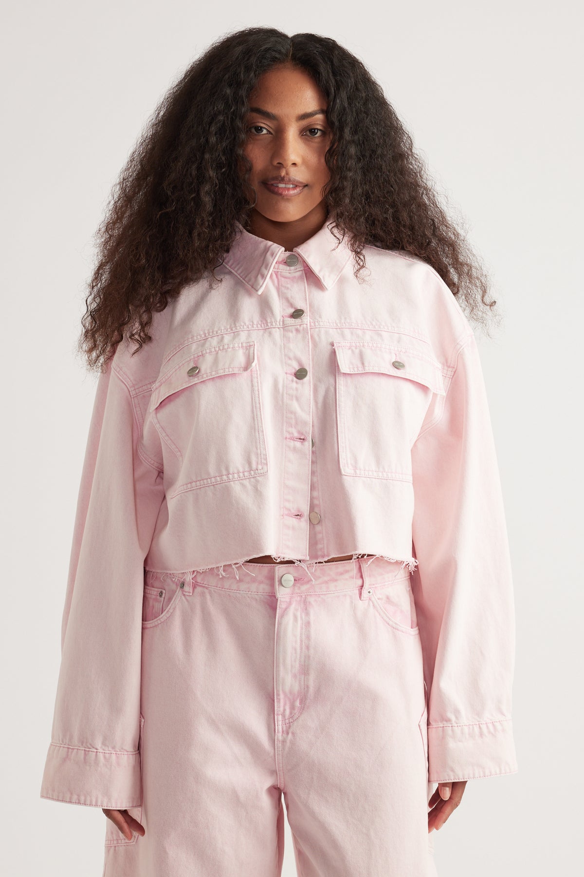 Woman wearing a cropped pink denim shirt with patch pockets and matching jeans