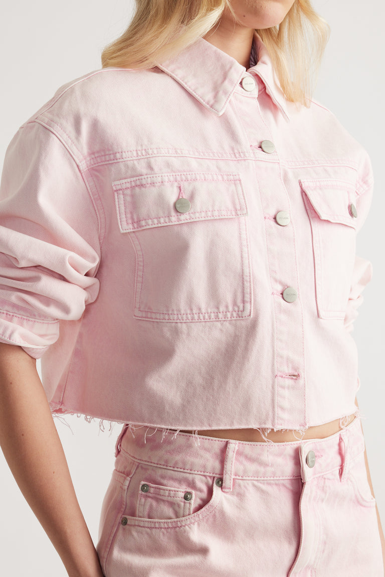 Woman wearing a cropped pink denim shirt with button front, patch pockets and a raw hem