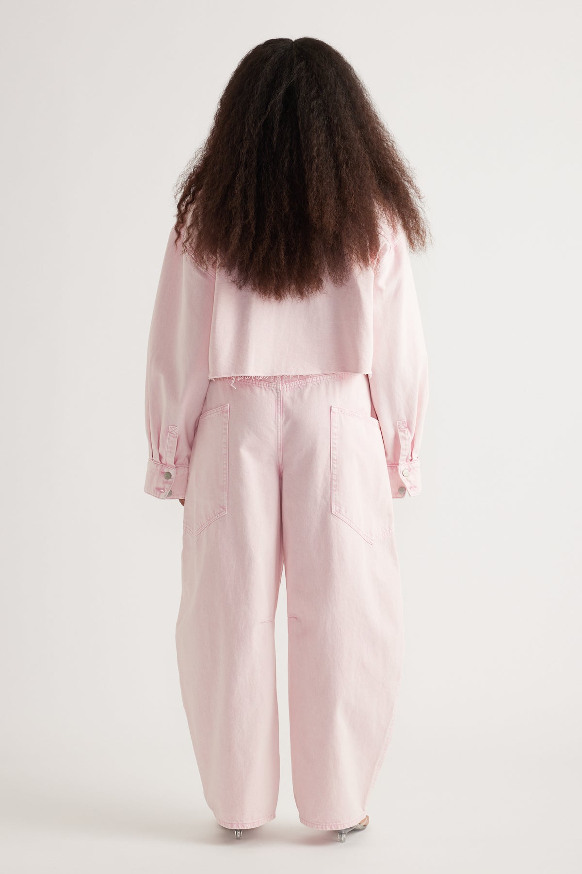 Back view of a model wearing a pale pink cropped denim shirt with long sleeves and matching wide-leg pants
