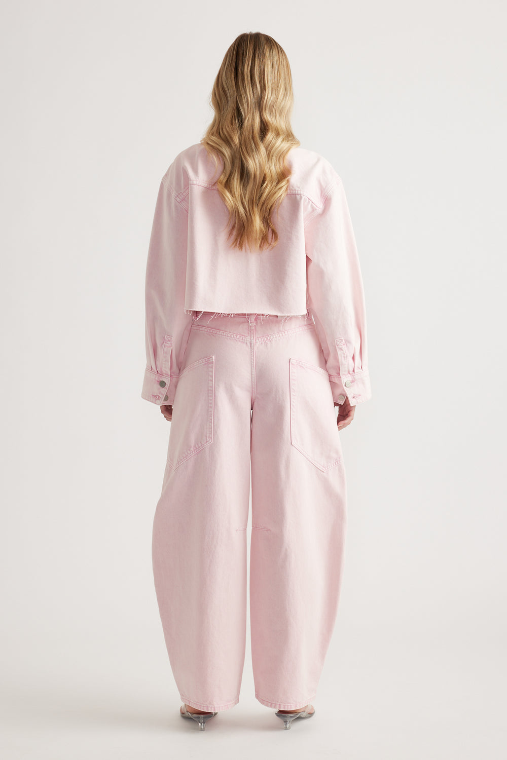 Back view of a woman wearing a cropped pink denim shirt with matching wide leg pants