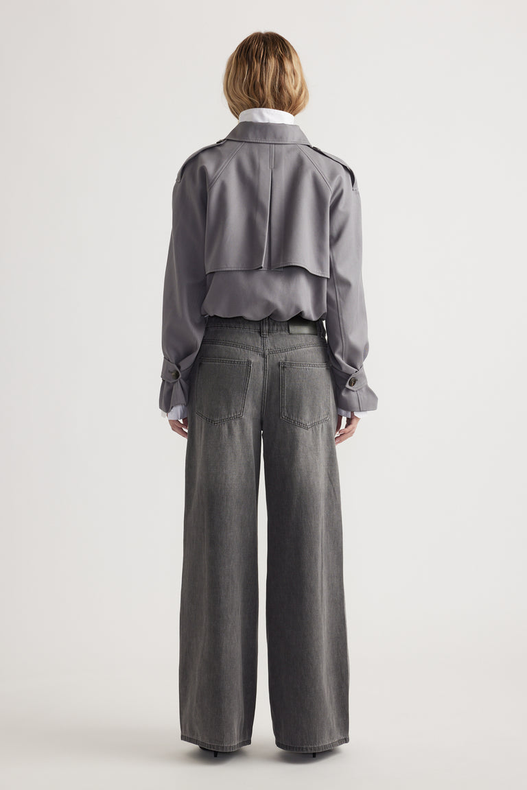 Woman wearing grey cropped jacket paired with mid-rise wide leg denim jeans, seen from behind on plain background