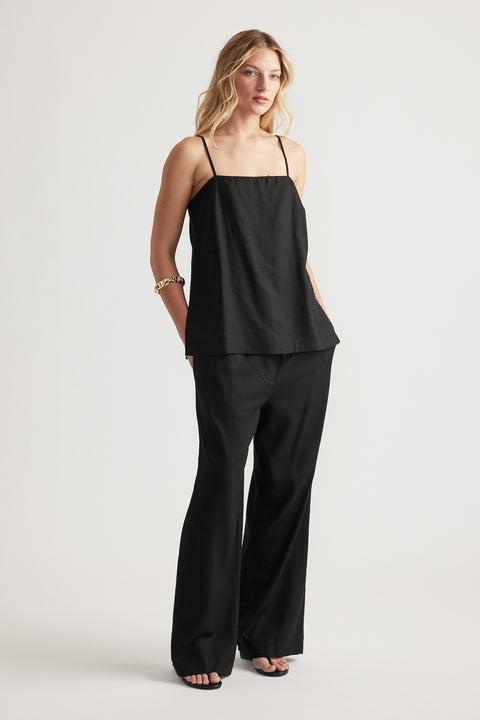 Woman wearing a black linen blend cami with thin straps paired with wide-leg black pants and a gold bracelet
