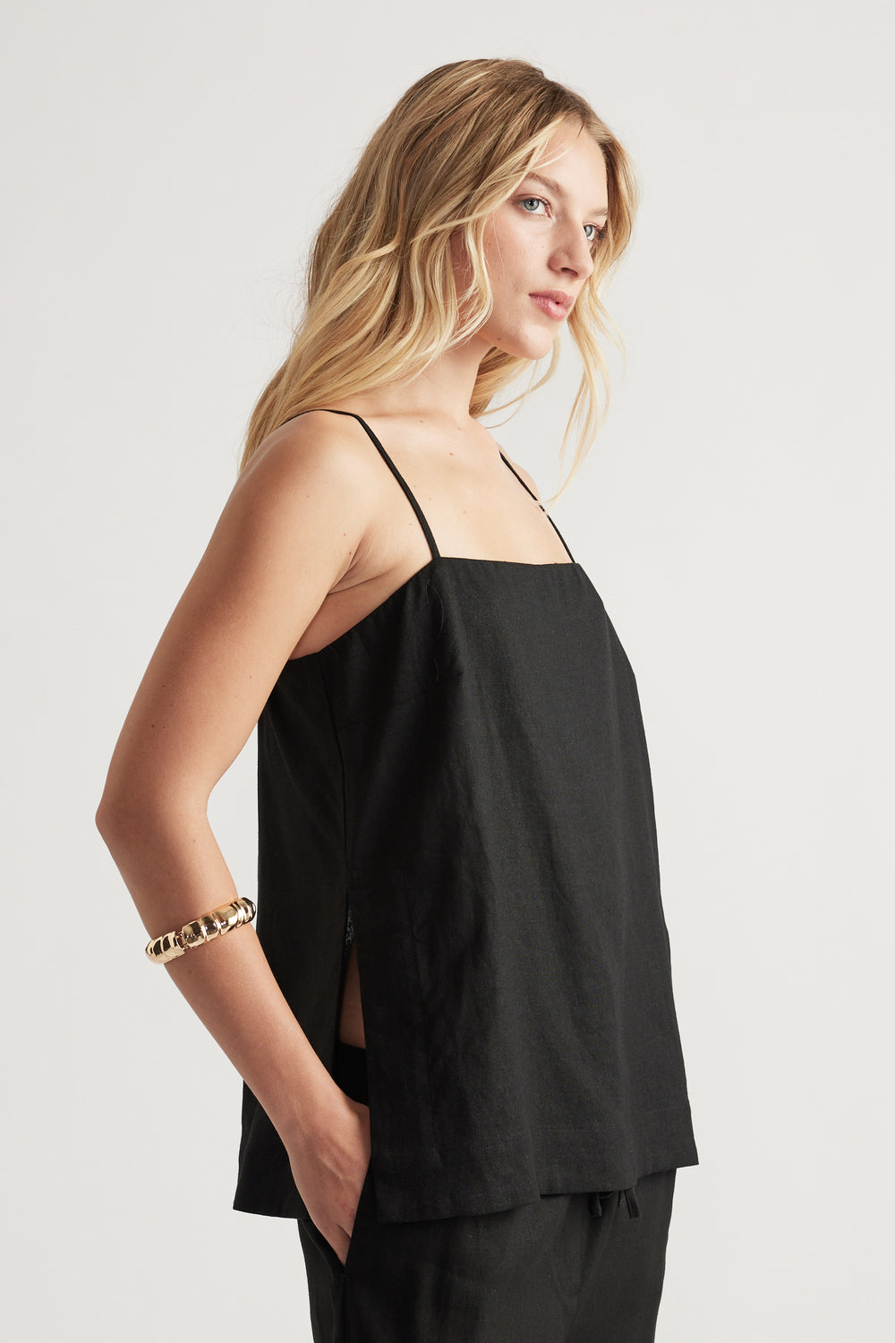Side view of woman wearing a black linen blend cami with thin straps and relaxed fit paired with matching pants