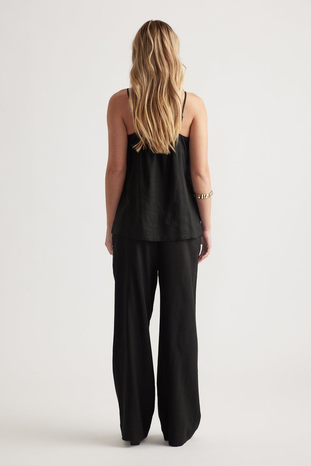 Woman with long blonde hair wearing a loose black linen blend cami and wide-leg pants in a minimalist setting