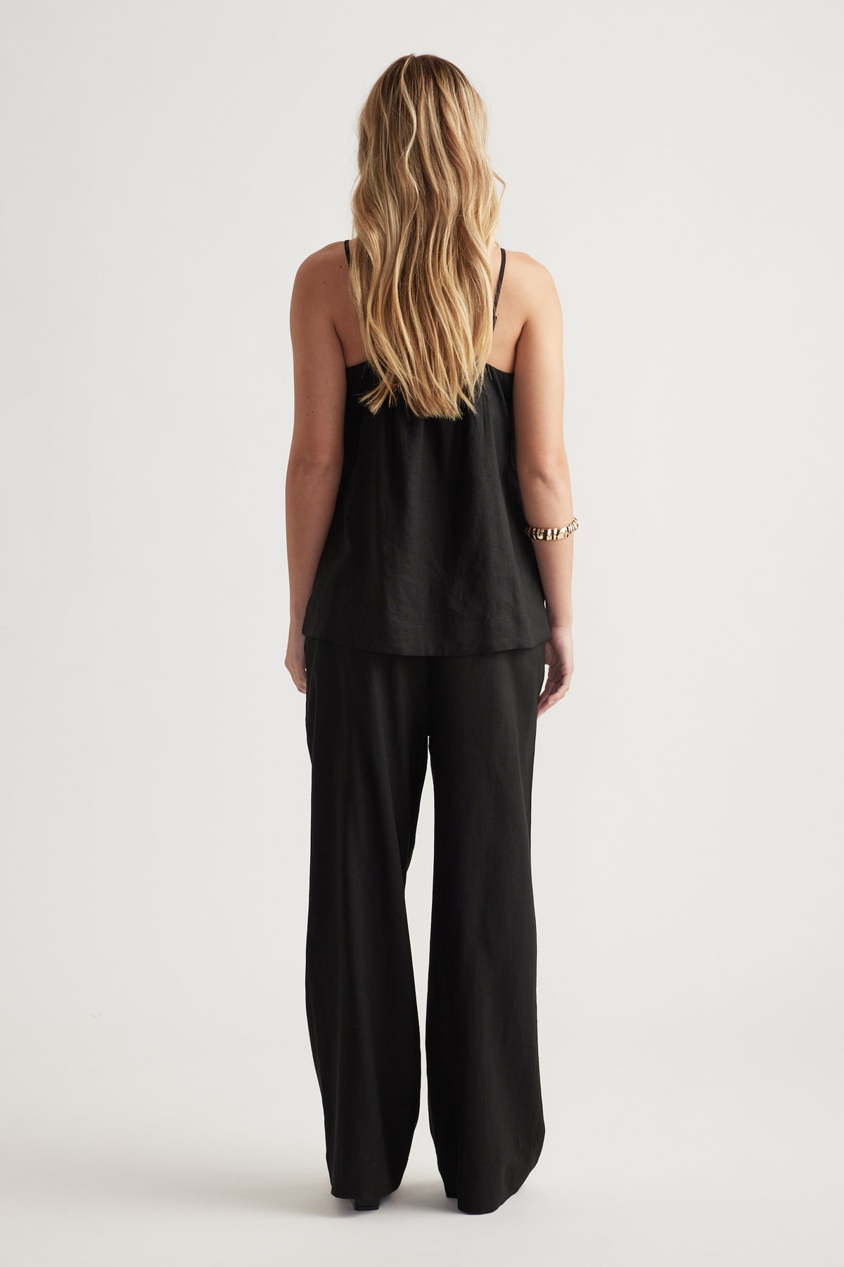 Woman with long blonde hair wearing a loose black linen blend cami and wide-leg pants in a minimalist setting