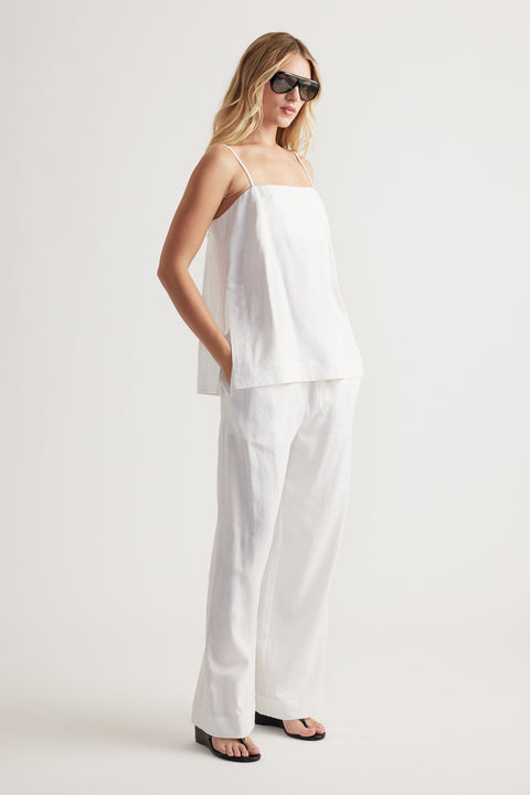 Woman wearing a loose white linen cami with thin straps paired with matching wide-leg linen pants and black sandals.