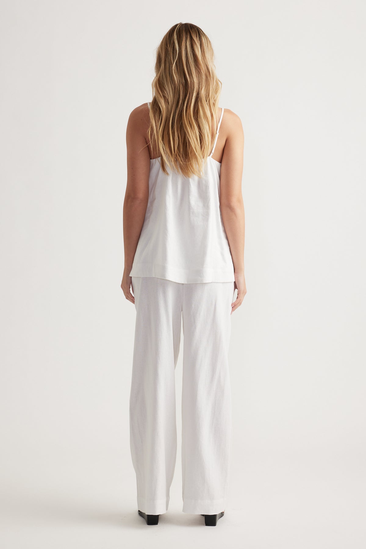 Woman wearing a relaxed white linen blend cami with wide-leg matching linen pants and black heels, seen from behind