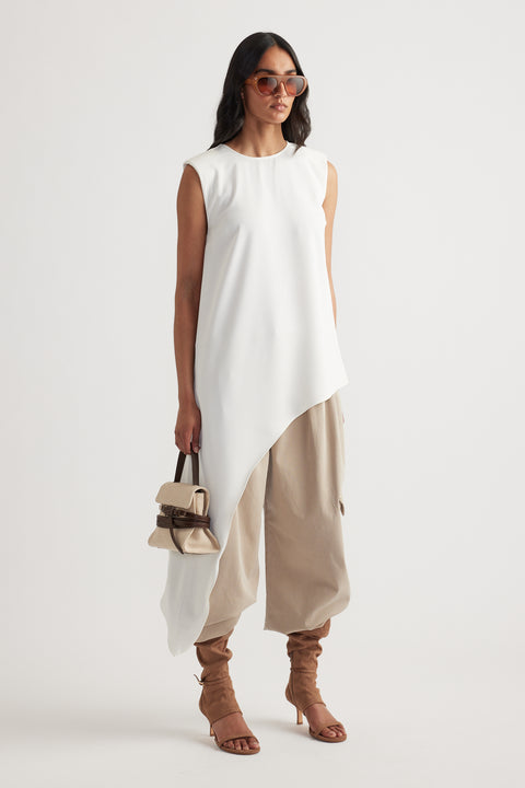 Woman wearing an ivory asymmetrical drape top paired with loose beige pants and tan heeled sandals carrying a small bag
