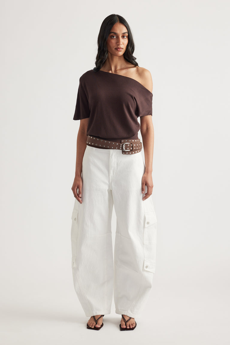 Woman wearing a brown asymmetric off shoulder knit top with white wide leg cargo pants, studded belt and sandals