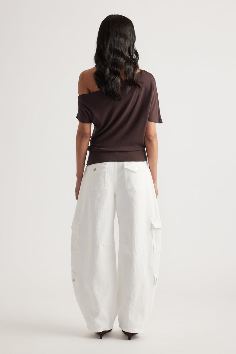 Back view of woman wearing a brown asymmetric off shoulder knit top with white wide-leg cargo pants