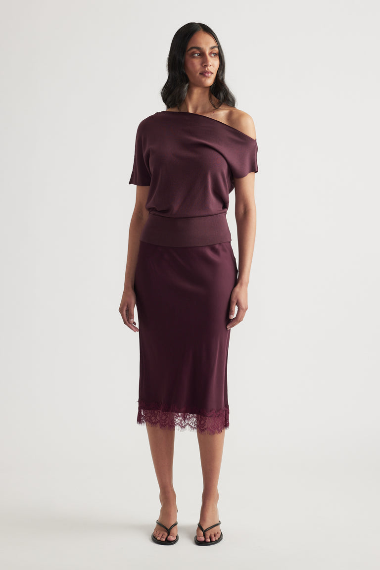 Woman wearing a burgundy off shoulder knit top with a matching midi skirt and lace hem, paired with strappy sandals