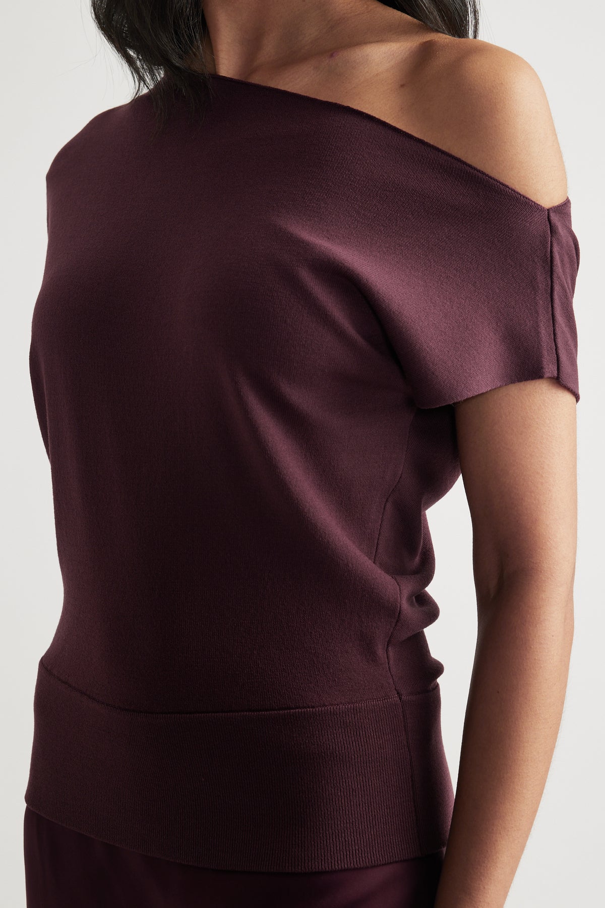 Woman wearing a burgundy off shoulder knit top with an asymmetric neckline and cinched hem