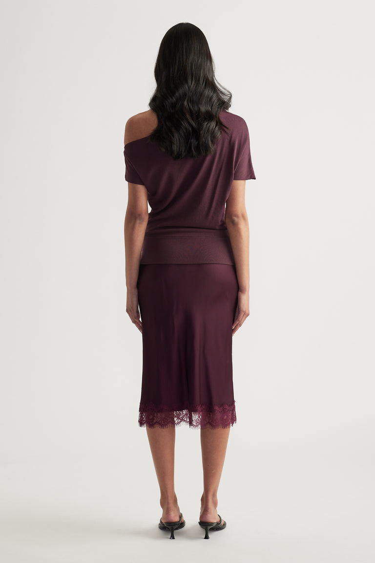 Back view of woman wearing a burgundy asymmetric off shoulder knit top with cinched hem and lace trimmed midi skirt