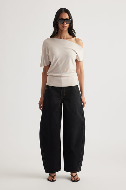 Woman wearing a light beige off shoulder knit top with cinched hem, black wide leg pants, sunglasses and sandals