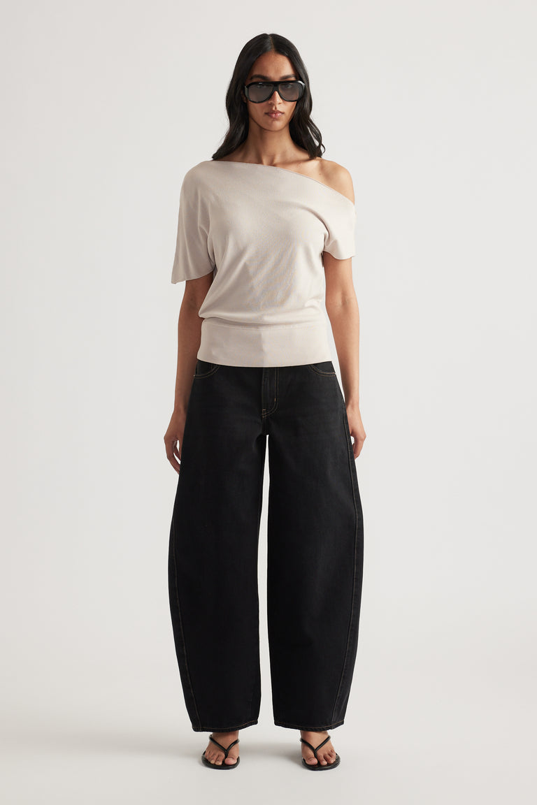 Woman wearing a light beige off shoulder knit top with cinched hem, black wide leg pants, sunglasses and sandals