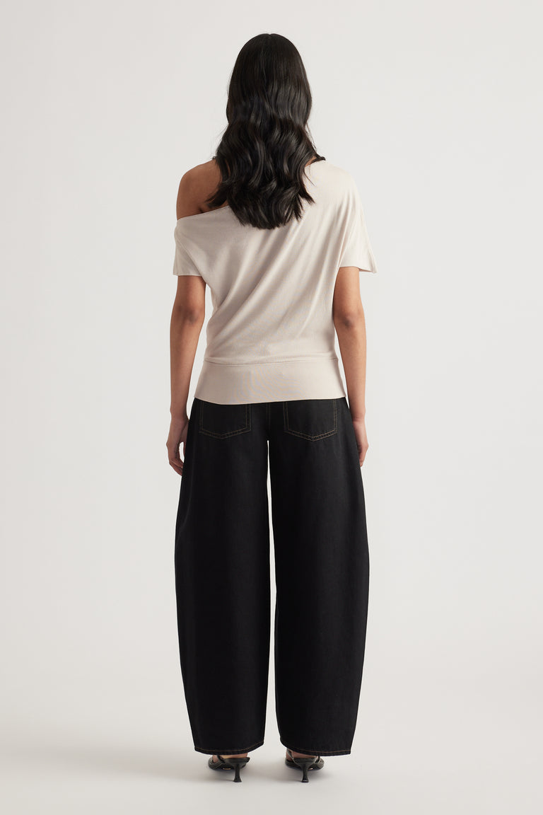 Woman wearing an asymmetric off shoulder cream knit top with cinched hem and black wide leg pants viewed from behind