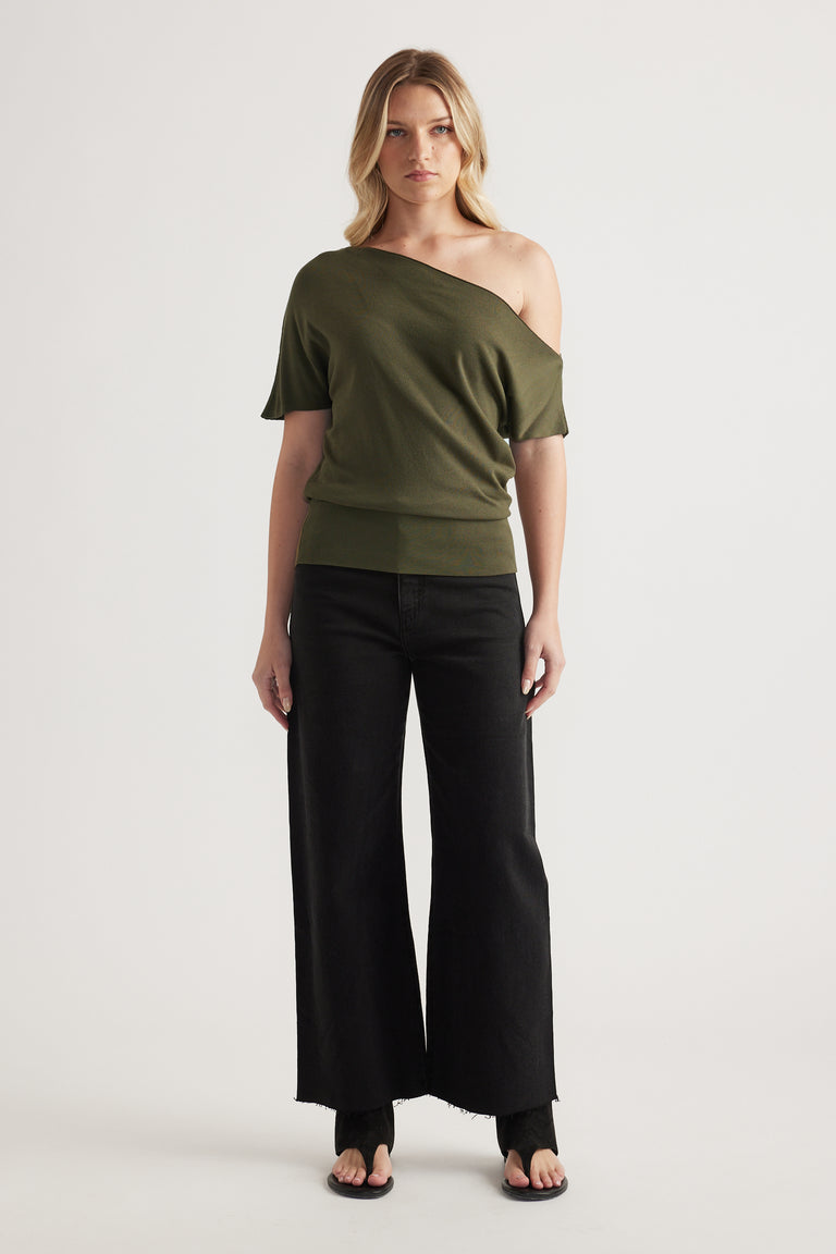Woman wearing an olive asymmetric off shoulder knit top with cinched hem, black wide leg pants and sandals