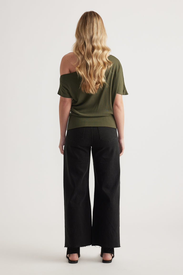 Back view of woman in an olive asymmetric off shoulder knit top with black wide leg pants and black sandals