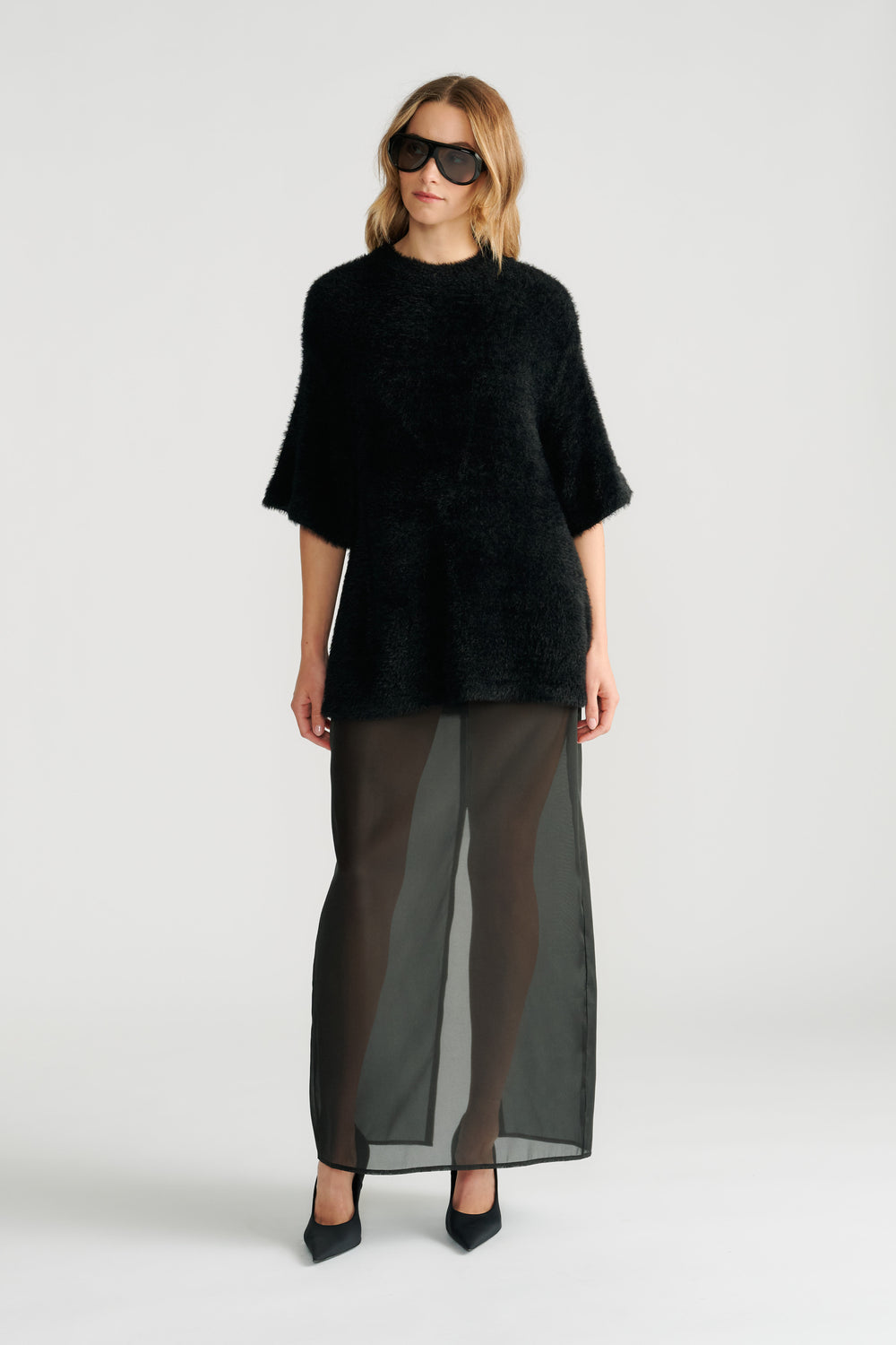 Woman wearing a textured black oversized knit tee paired with a sheer black maxi skirt and pointed heels.