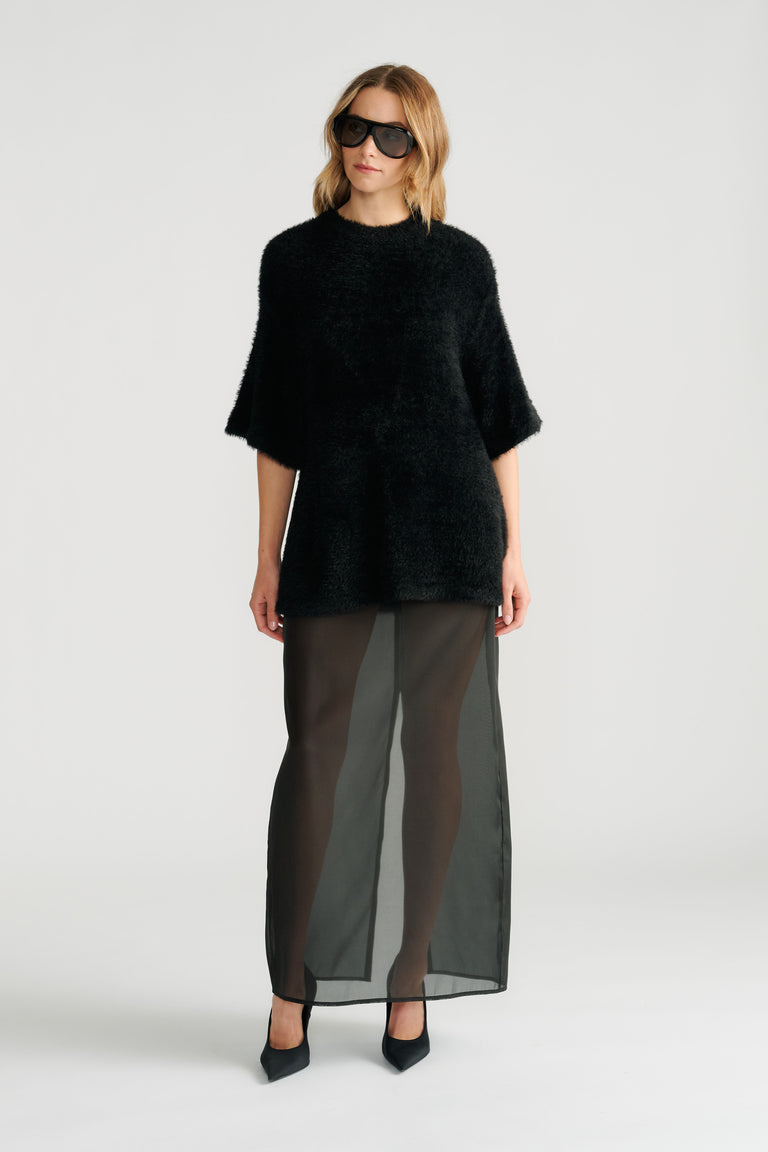 Woman wearing a textured black oversized knit tee paired with a sheer black maxi skirt and pointed heels.