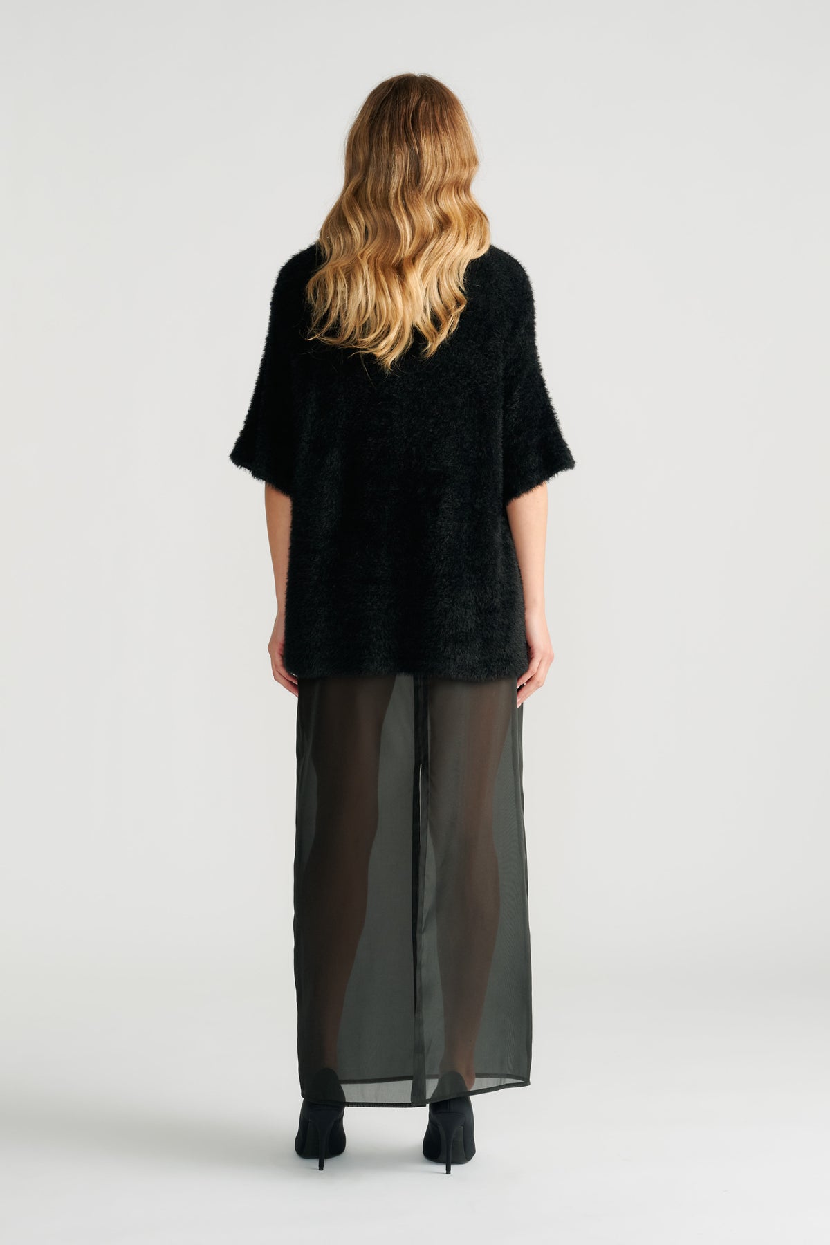 Back view of woman wearing a black oversized knit top paired with a sheer black maxi skirt and black heels.