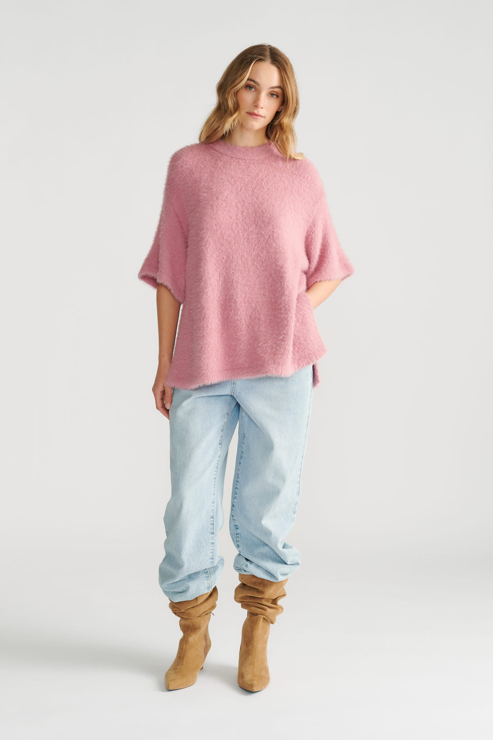 Woman wearing a soft pink oversized knit tee paired with loose light wash jeans and slouchy tan suede boots.