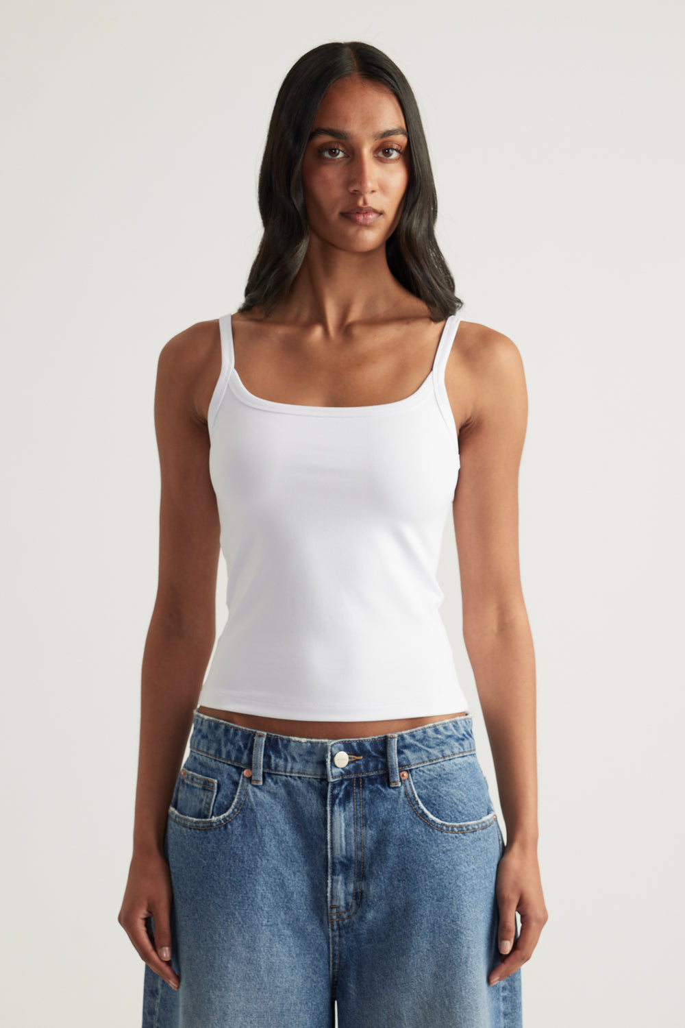 Woman wearing a white fitted thin strap tank top with blue denim jeans