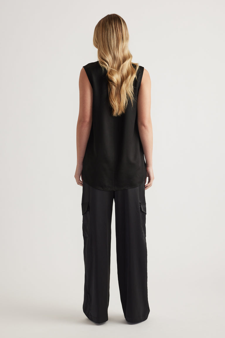 Back view of model wearing a black satin sleeveless tank with a high neckline and wide leg cargo pants