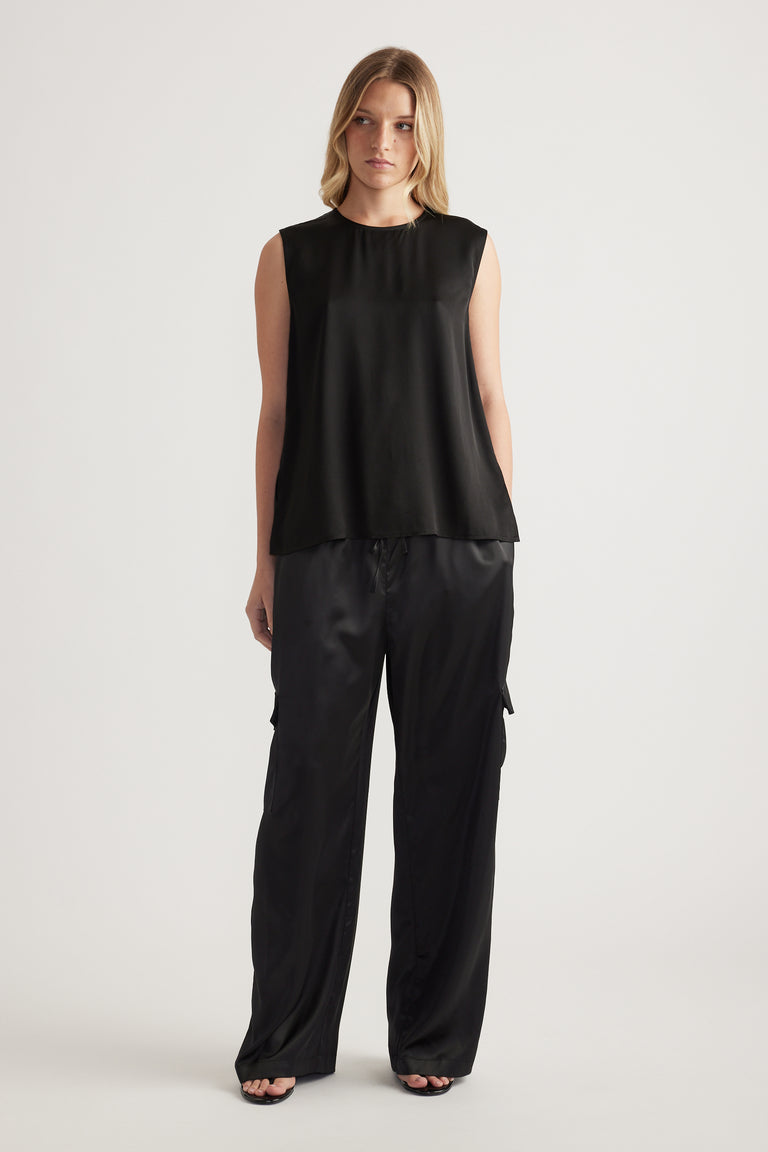 Woman wearing a black sleeveless satin tank with a high neckline and relaxed black cargo pants