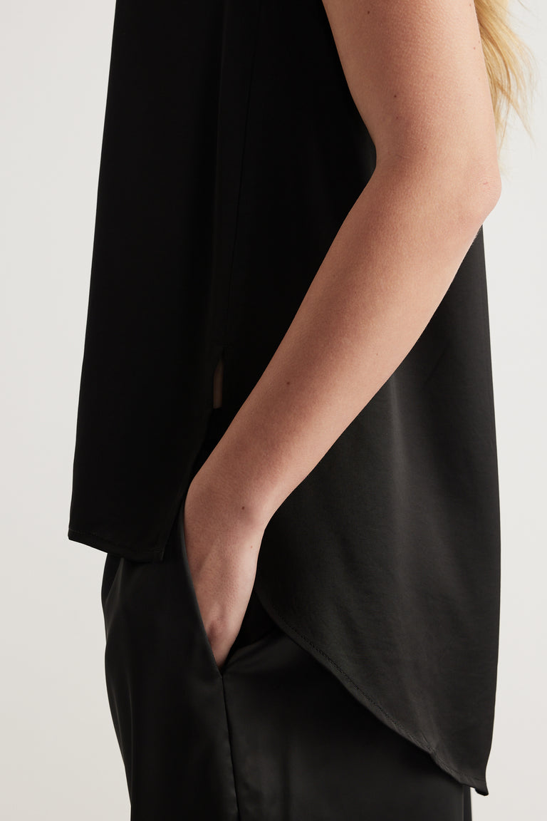 Woman wearing a black satin sleeveless top with a relaxed silhouette and curved hem