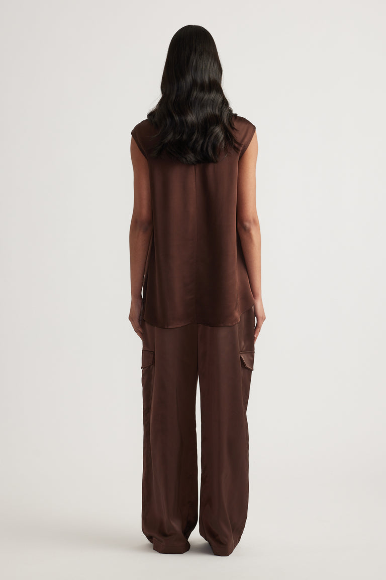 Back view of a woman wearing a brown satin sleeveless top with a high neckline and relaxed cargo pants