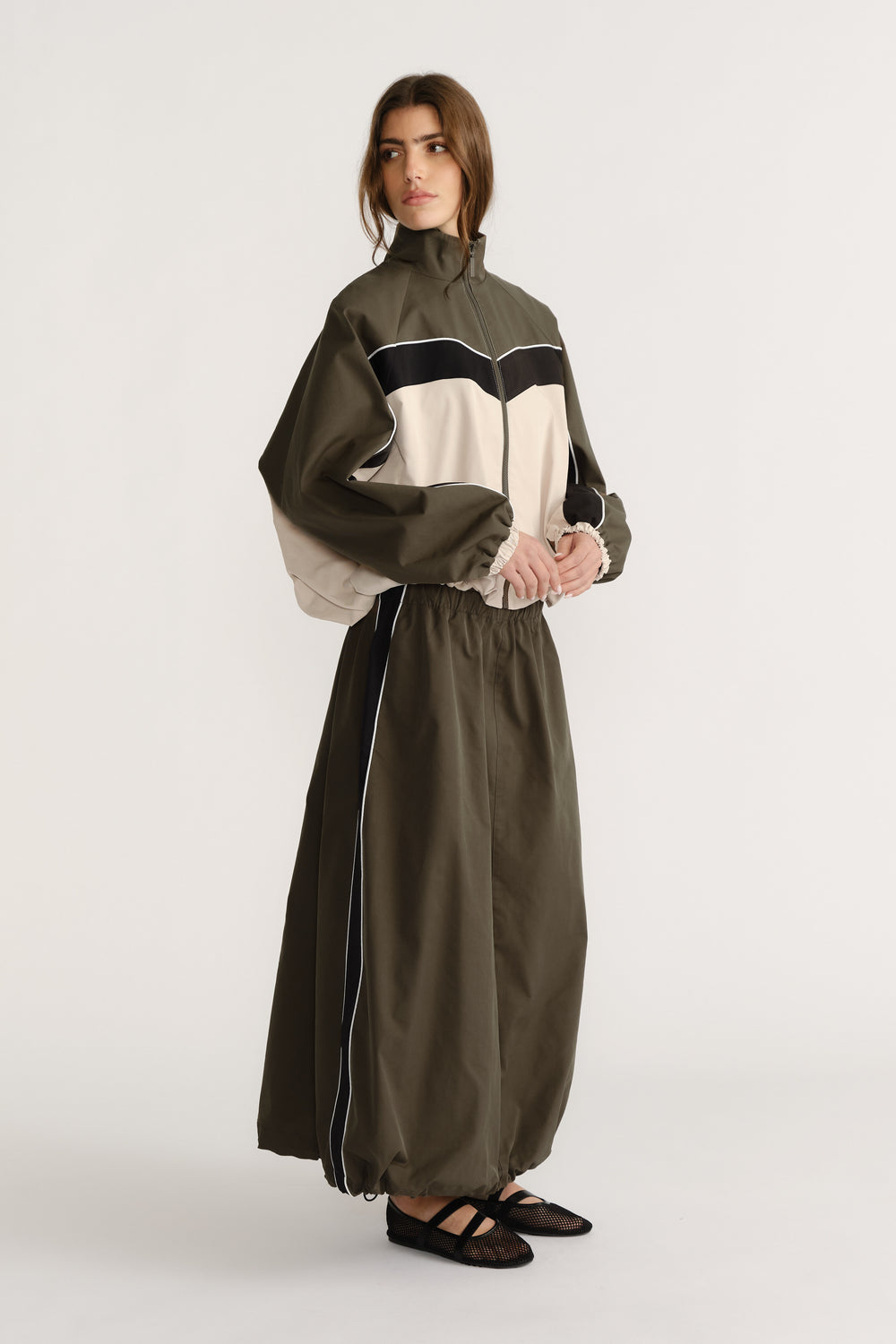 Woman wearing an olive green and beige contrast panel jacket paired with a high-waisted ankle-length skirt