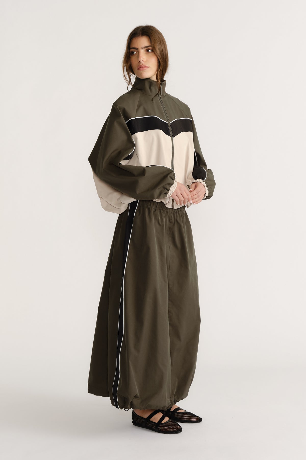 Woman wearing an olive green and beige contrast panel jacket paired with a high-waisted ankle-length skirt