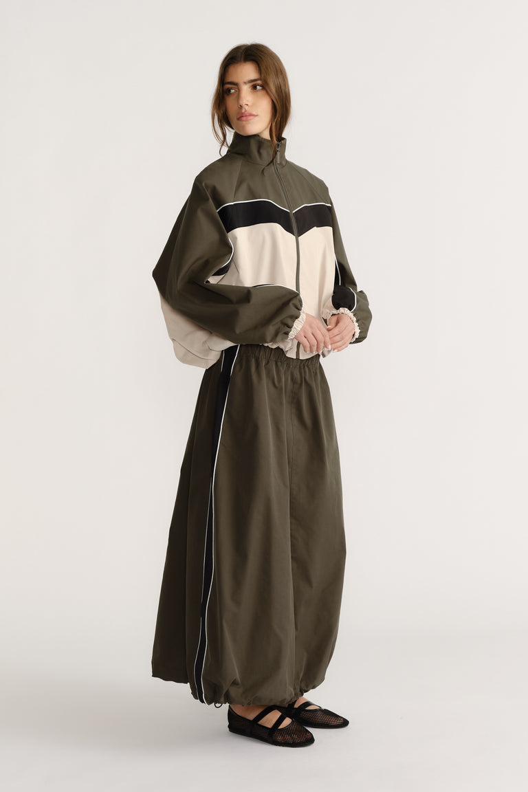 Woman wearing an olive green and beige contrast panel jacket paired with a high-waisted ankle-length skirt