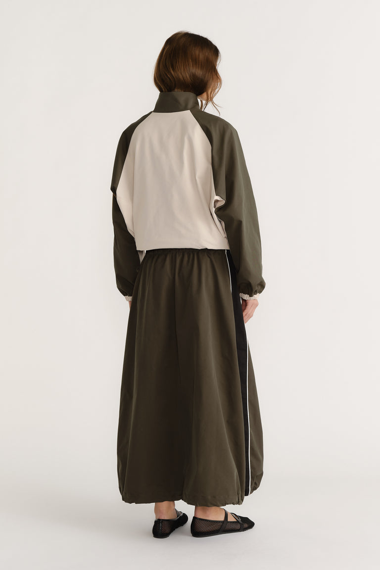 Rear view of woman wearing ankle-length cocoon skirt with elasticated waist and color block long-sleeve jacket