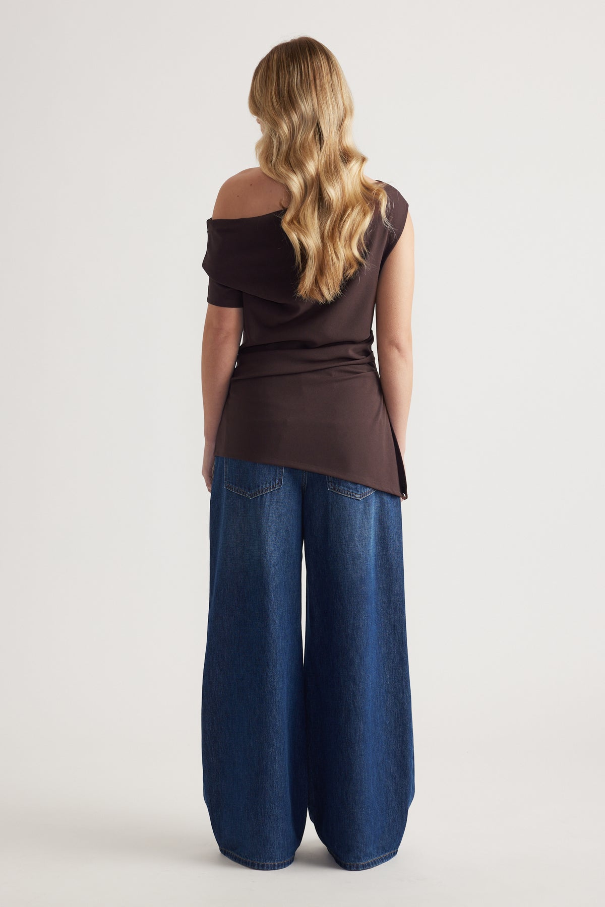 Woman seen from behind wearing a dark off shoulder asymmetric top with wide leg jeans