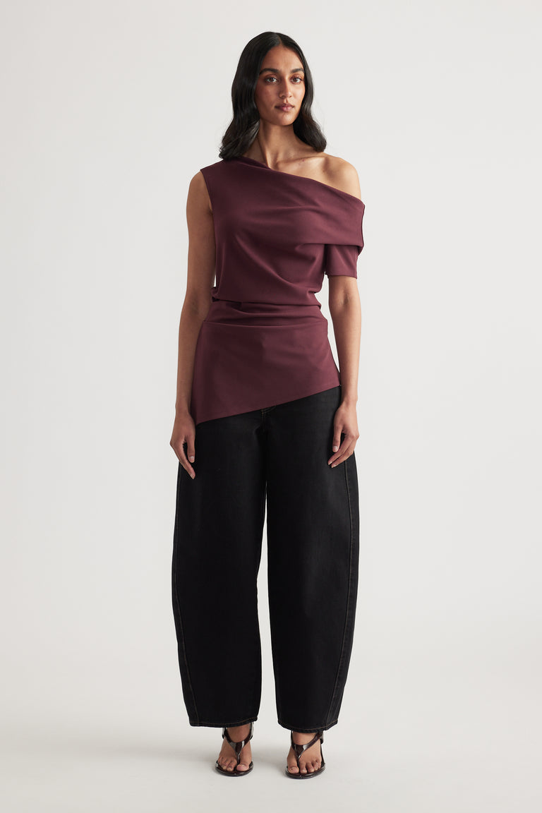 Woman wearing a burgundy off shoulder asymmetric top with crossover detail, black wide leg pants and sandals