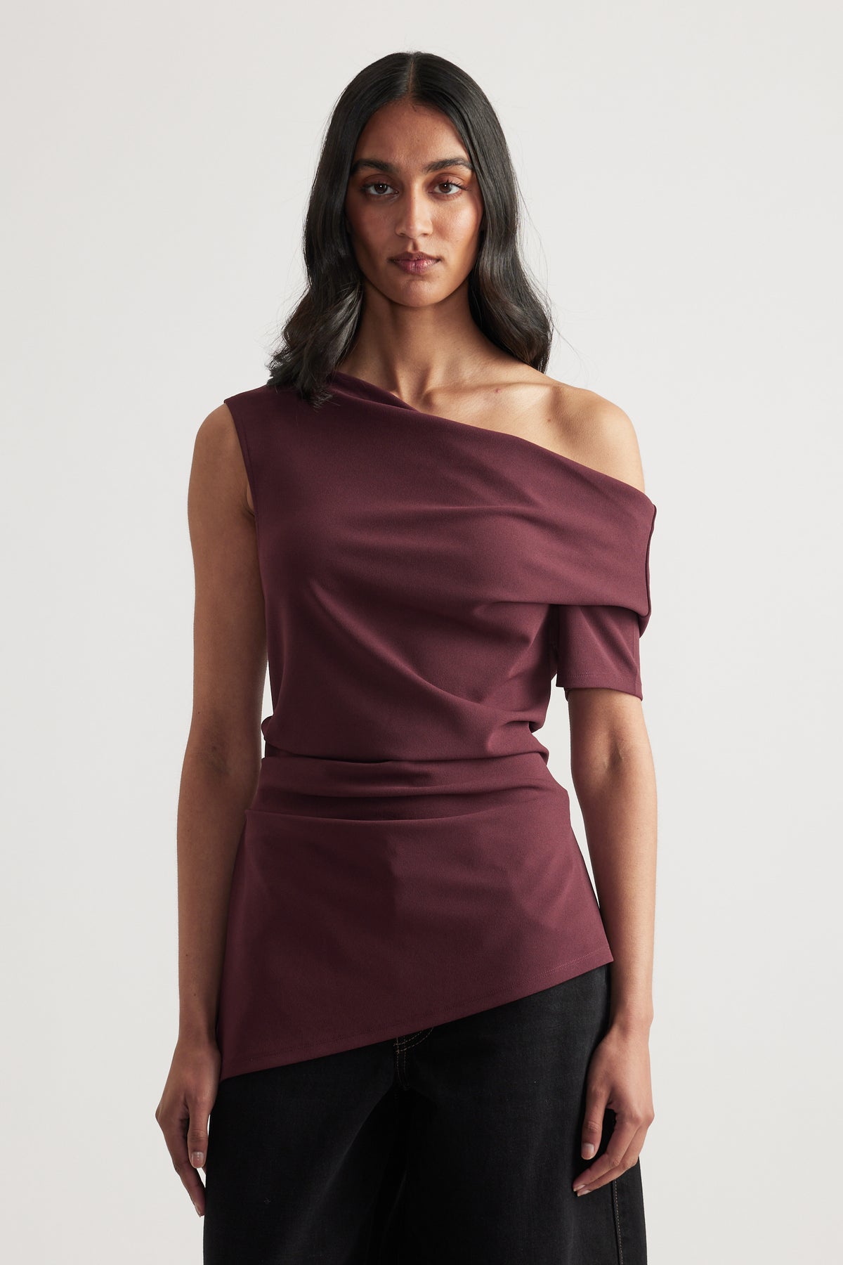 Woman wearing a burgundy asymmetric off shoulder top with black pants