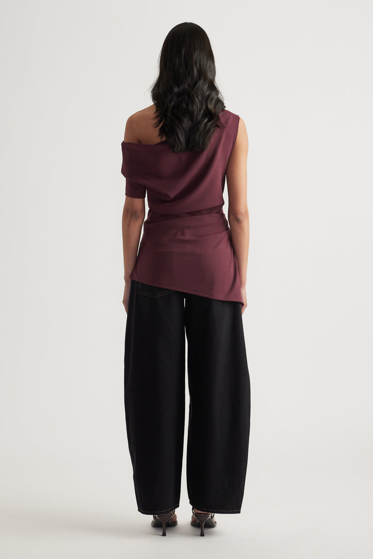 Woman seen from behind wearing a burgundy asymmetric off shoulder top with black wide-leg pants