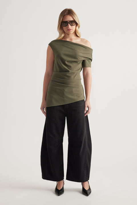 Woman wearing an olive off shoulder top with an asymmetric neckline and black wide leg pants