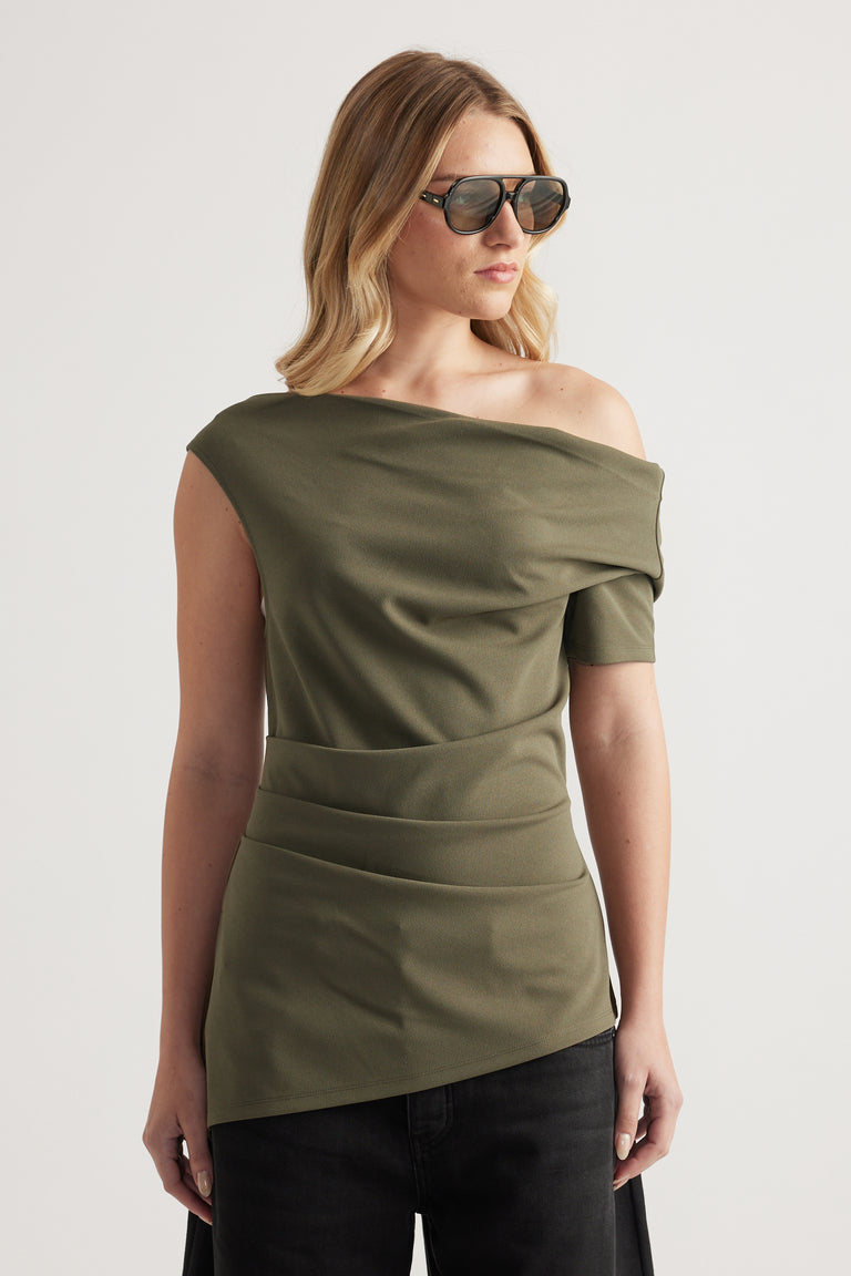 Woman wearing an olive asymmetric off shoulder top with crossover draping, black jeans and sunglasses